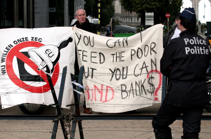 Banner utanfor et EU-møte i Brussel i forbindelse med Hellas sine økonomiske utfordringer, som lyder « Dere kan ikke gi folket mat, men dere kan finansiere bankene? » 																															Foto AP Photo/Yves Logghe