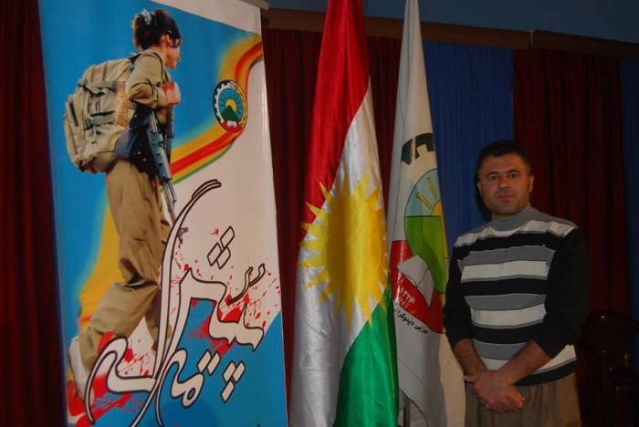 Anwar Mohamadi foran PDKIs flagg, det kurdiske flagget og en plakat av en peshmergasoldat. Foto: Privat