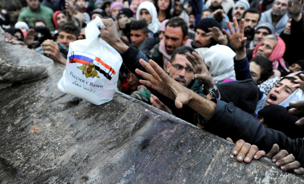 Syrere som er evakuert fra øst-Aleppo, strekker seg etter mat fra Russland, med opskriften « Russland er med deg ». 					Foto Reuters/Omar Sanadiki
